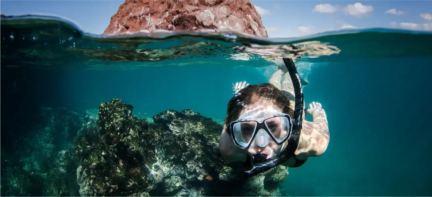 Snorkeler exploring clear turquoise waters and volcanic rock formations in the Galapagos Islands, enjoying a tropical marine adventure.