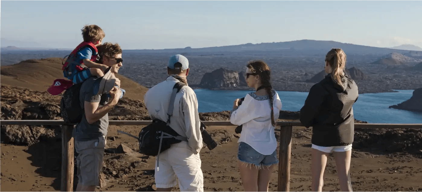 A family listening to the Galápagos Islands naturalist guide, while other travelers enjoy the view of the Enchanted Islands.