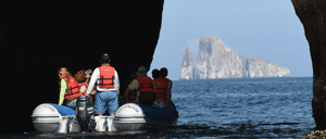 Cerro Brujo - San Cristobal in Galapagos Islands, rock formations with Kicker rock at background and tourist in panga