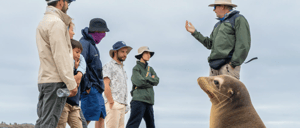 A Galapagos guide, travelers and a sea lion listening the explanation about the North Seymour Island