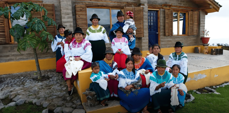 Karanki Magdalena community members in traditional Andean clothing, posing in front of an adobe house.